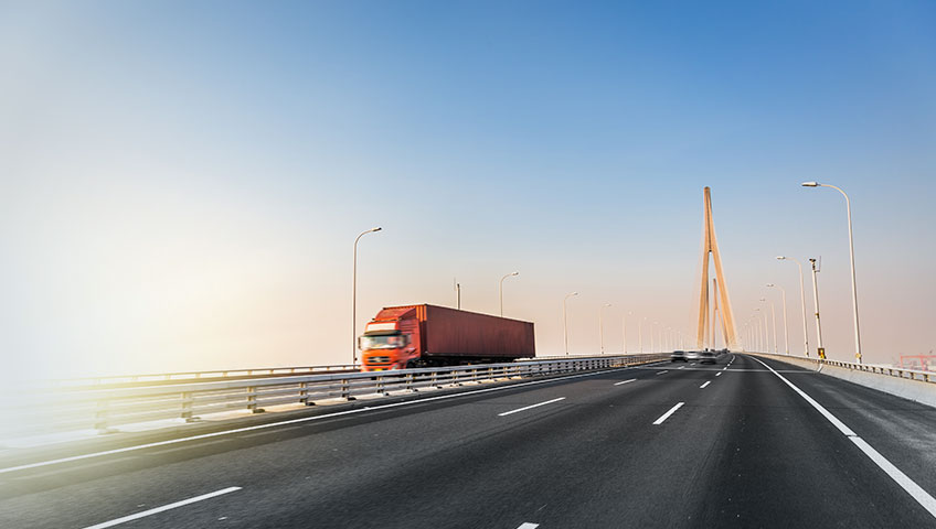 A red truck driving down the road near a bridge.