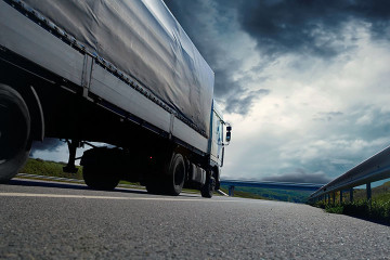A truck driving down the road under a cloudy sky.