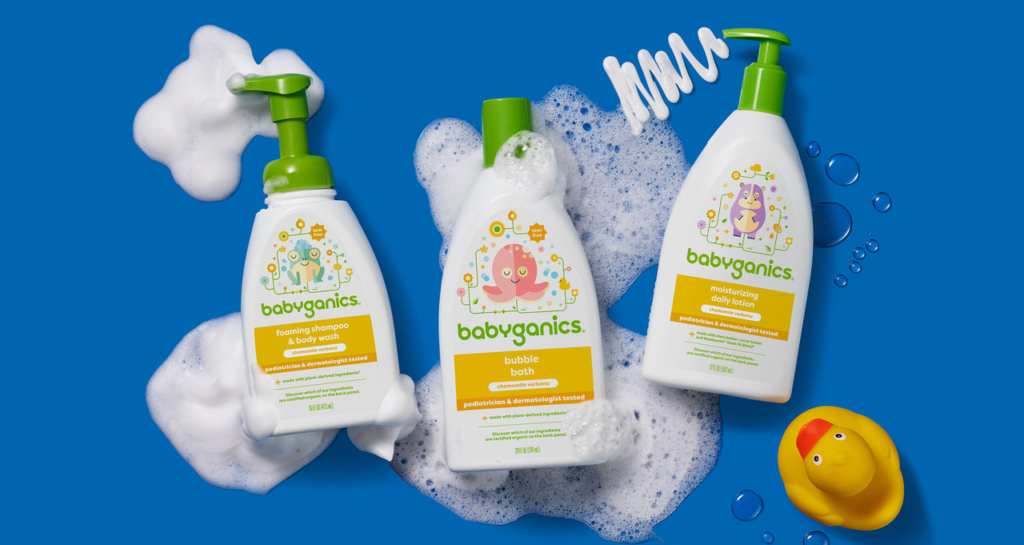 Image shows three bottles of Babyganics baby care products arranged on a blue background. The bottles are for foaming shampoo and body wash, bubble bath, and moisturizing daily lotion. The bottles feature pastel colors and the Babyganics logo